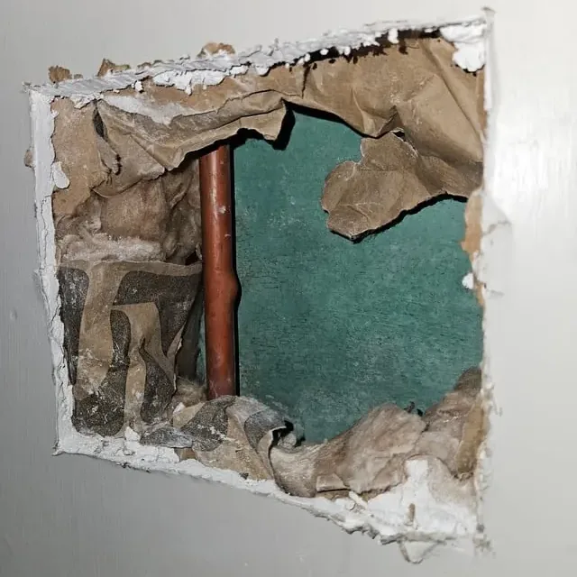 Drywall opened to reach a leaking copper pipe inside the wall