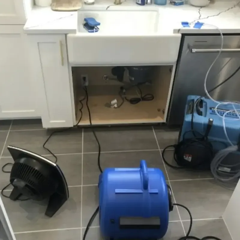 Air movers drying under a kitchen sink cabinet after an appliance leak