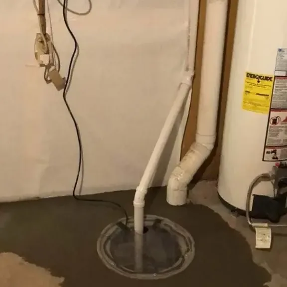 Basement sump pit and discharge pipe with a wet concrete floor beside a water heater