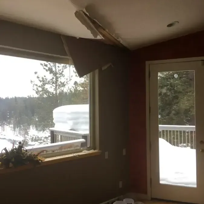 Top-floor room with the ceiling torn open and snow outside the window after an ice dam leak