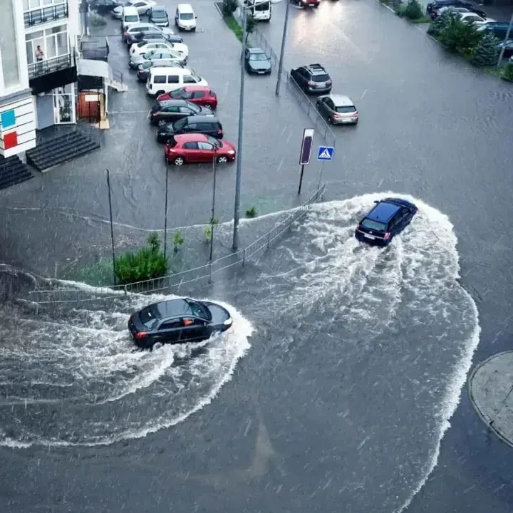 Floodwater covering a street and parking area with cars driving through it